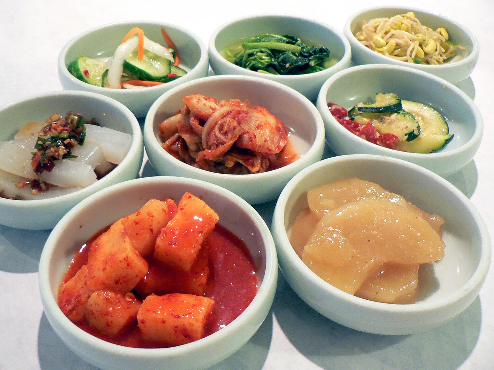 Small bowls of Korean banchan including kimchi, bean sprouts, radish, and seasoned vegetables