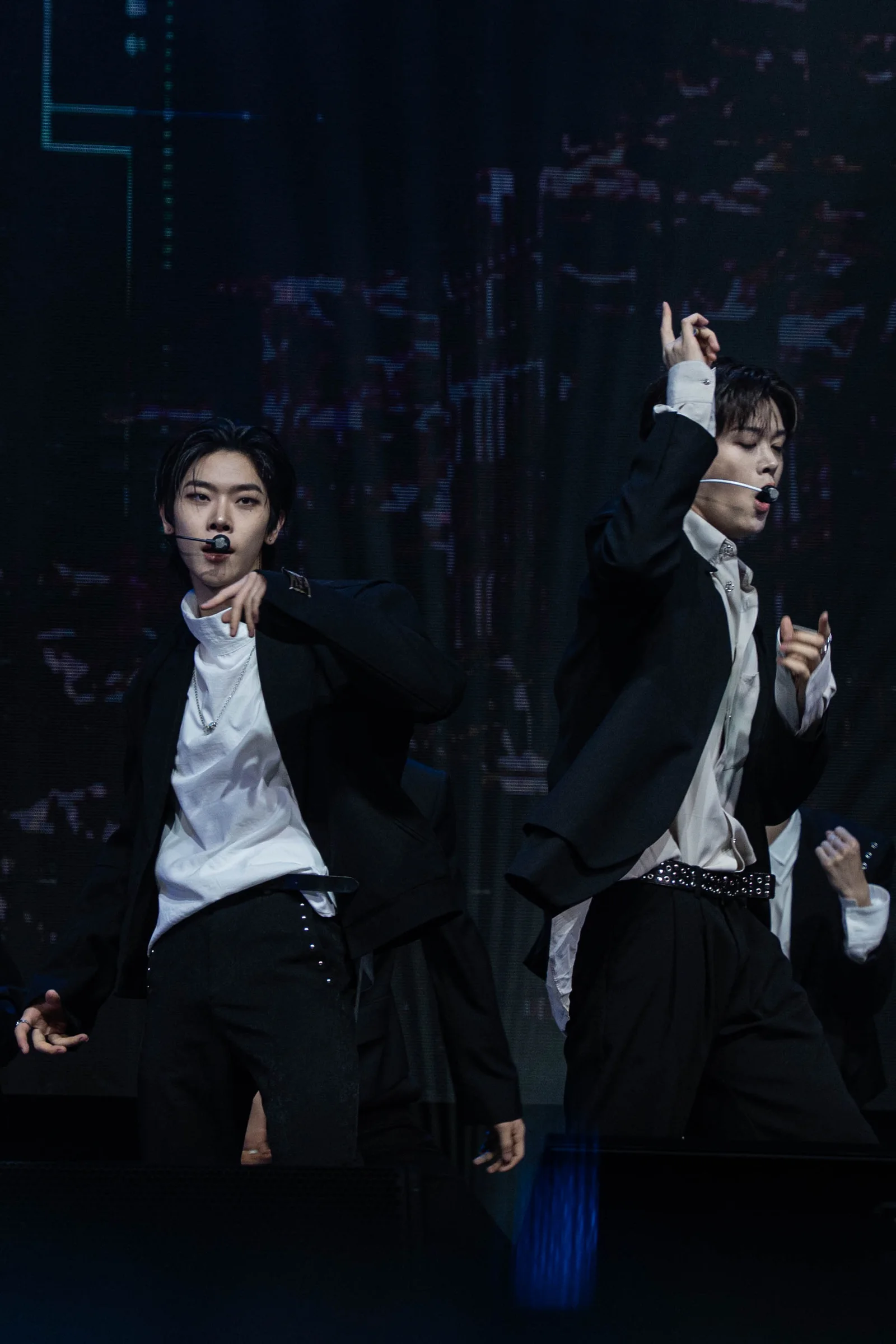 Two Close Your Eyes members performing with headset microphones on a dark concert stage