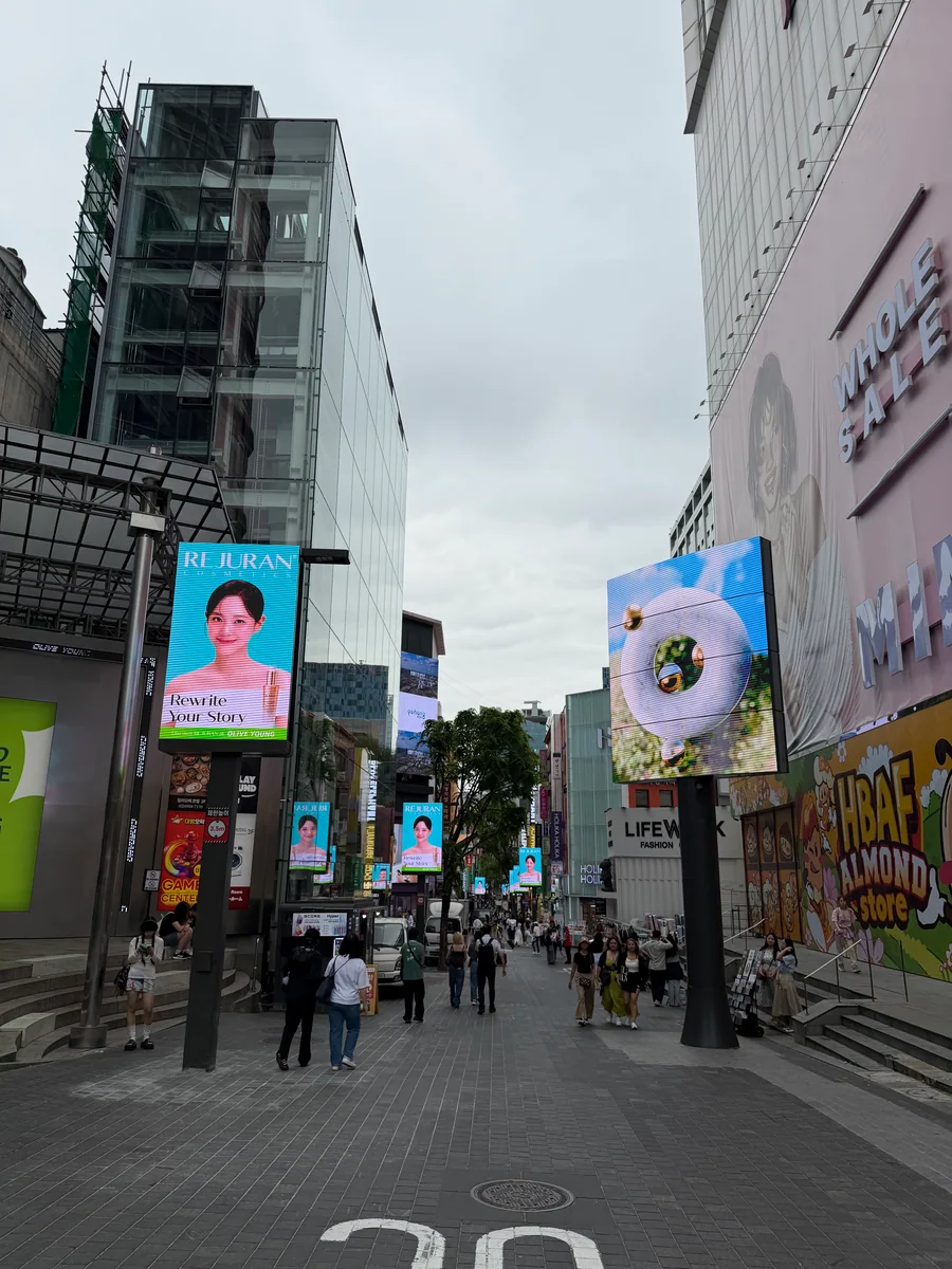 Pedestrians, storefronts, and large digital displays on Myeongdong street in central Seoul